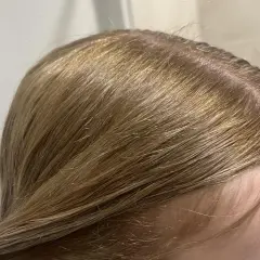 Zbliżenie na blond włosy z widocznymi pomarańczowymi tonami przy skórze głowy.