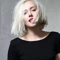 Blonde Frau mit einem geraden Bob und rotem Lippenstift, die provokativ in die Kamera blickt.