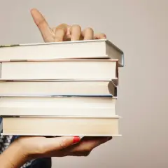 Main tenant une pile de livres, le doigt levé comme pour indiquer un titre. Chaque livre a son propre isbn.