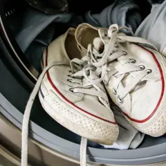 Weiße Turnschuhe mit roten Streifen liegen in der Waschmaschine, bereit zum Laufschuhe waschen.