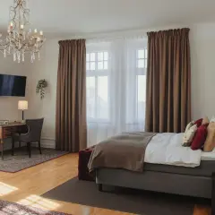 Ett elegant hotellrum på hotel Drott Karlstad med en stor säng, skrivbord och kristallkrona.