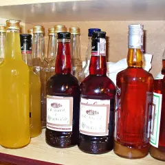 Rząd butelek z różnymi alkoholami, w tym żółtymi nalewkami i ciemnymi, jak czarna wódka.