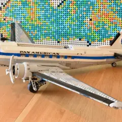 Ein detailreiches Lego DC-3 Flugzeug der Pan Am steht auf einem Holzboden, im Hintergrund eine bunte Lego-Weltkarte.