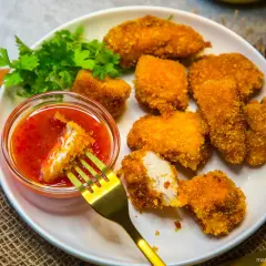 Knusprige Hähnchen-Nuggets, die man einfach selber machen kann, mit süß-saurer Soße und frischer Petersilie. Ein roter Chili liegt daneben.