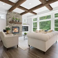 Cozy living room with a stone fireplace, tufted sofa, and an accent ceiling with exposed wooden beams.