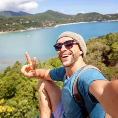 Szczęśliwy mężczyzna robi selfie na tle tropikalnej zatoki. Idealne wakacje dla singli, pełne słońca i przygód.