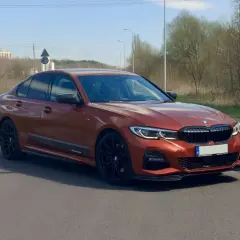 Pomarańczowe BMW 330i G20 na drodze, z widocznymi czarnymi felgami i detalami aerodynamicznymi.