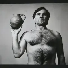 Józef Robakowski, nagi mężczyzna z krzaczastą klatką piersiową, trzyma w dłoni gliniany dzban.
