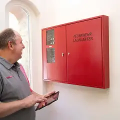 Mann prüft mit Tablet die Brandmeldeanlage. Regelmäßige Wartung sorgt für Sicherheit.