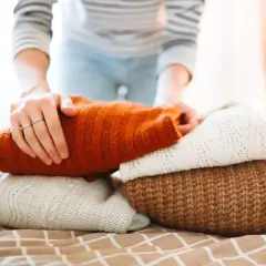 Hände falten gestapelte Pullover. Die warme Wolle duftet nach frischem Waschmittel, bereit für den Kleiderschrank.