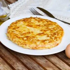 Frittata di patate dorata su piatto bianco, con cipolla, uova e olio d'oliva come ingredienti.
