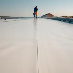 Arbeiter auf einem hellen Flachdach, das für die Windsogsicherung vorbereitet wird.