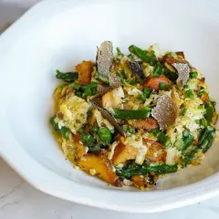 Delicioso revuelto de cantharellus con espárragos, trufa negra y cebollino, servido en un plato blanco.