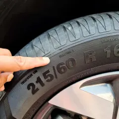 Palec wskazuje na oznaczenia opon: 215/60 R16. Informacje te pomagają dobrać odpowiednie ogumienie.