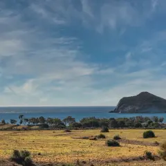 Paisaje árido del desierto Cabo de Gata con mar azul y una isla rocosa al fondo.