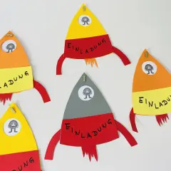 Bunte Raketen zum raketen einladung basteln, jede mit einem kleinen Monster im Fenster und dem Wort "Einladung" auf gelbem Band.