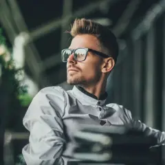 Florian, młody mężczyzna w okularach, w białej koszuli, spogląda w bok, zamyślony.