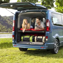 Para relaksuje się w kamperze Opel Vivaro, z widokiem na rzekę i kemping.