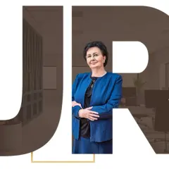 Kobieta w niebieskiej marynarce na tle biura, z literami JR.