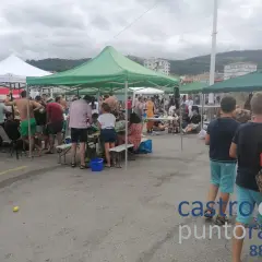 Gente reunida bajo carpas en un evento al aire libre en **Santa Ana, Castro Urdiales**. Un día nublado con ambiente festivo.