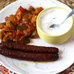 Dos salchichas merguez que es picantes, acompañadas de un guiso de verduras y una salsa cremosa.