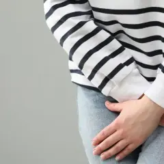 Kobieta w bluzie w paski i jeansach trzyma dłonie na podbrzuszu, sugerując dyskomfort. Szuka silnego leku na zapalenie pęcherza bez recepty.