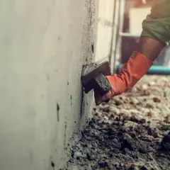 Pracownik w pomarańczowych rękawicach tynkuje ścianę. Brak zgody sąsiada na ocieplenie budynku może opóźnić prace.