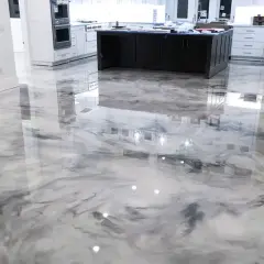 Un moderno pavimento epossidico con un effetto marmorizzato bianco e grigio riflette le luci e l'arredamento della cucina.
