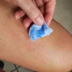 Mano che pulisce la pelle con un dischetto di cotone blu, mostrando come togliere la vernice dalla pelle in modo efficace.