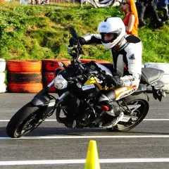 Motocyklista w białym kasku i kombinezonie doskonale opanował pozycję na motocyklu, pochylając się na zakręcie toru.