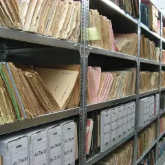 Rzędy półek archiwum wypełnione teczkami i pudłami. Na jednej z teczek widoczna jest sygnatura: "11497/58".