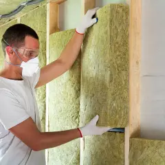 Un ouvrier installe un panneau d'isolation minérale dans une structure murale en bois, respectant les normes d'isolation des murs RT 2020.