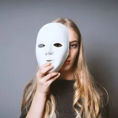 Ragazza bionda con maschera bianca, un'espressione che evoca il significato istrionico, nascondendo parte del volto.