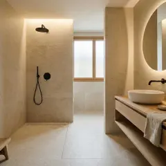 Un baño moderno con ducha empotrada, lavabo sobre mueble de madera y espejo circular iluminado, evocando la serenidad de los baños japoneses.