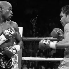 Floyd Mayweather Jr. in his signature defensive stance, facing Manny Pacquiao in a boxing ring.