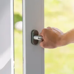 Dłoń chwyta metalową gałkę drzwi, otwierając je na zielony ogród.