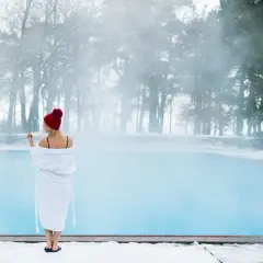 Kobieta w szlafroku i czapce stoi przy basenie w zimowy dzień. Czy basen stelażowy można zostawić na zimę?