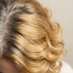 Zbliżenie na blond włosy z widocznymi ciemnymi odrostami i siwizną.