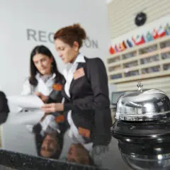 Recepcjonistki w hotelu omawiają dokumenty. Dzwonek hotelowy na pierwszym planie. Zwroty po angielsku w hotelu na recepcji są kluczowe.