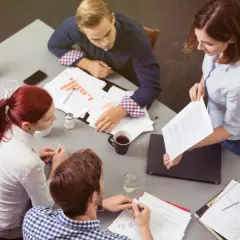 Vier Personen besprechen Dokumente und Diagramme. Sie zeigen **soziale Intelligenz** im Austausch von Ideen und im gemeinsamen Arbeiten.
