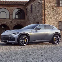 Srebrny Ferrari SUV Purosangue zaparkowany przed kamiennym budynkiem z łukowymi oknami.