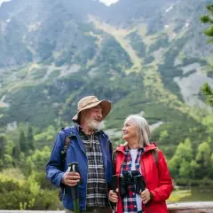 Szczęśliwa para seniorów na wczasach ze związku emerytów, podziwiająca górski krajobraz z jeziorem.