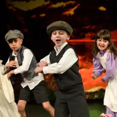 Dzieci w strojach teatralnych tańczą na scenie.