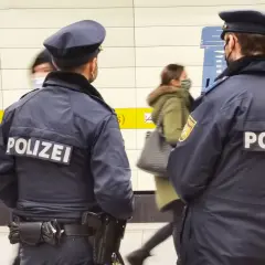 Zwei Polizisten stehen in einer U-Bahn-Station. Im Hintergrund sind 53 Personen zu sehen, die sich bewegen.