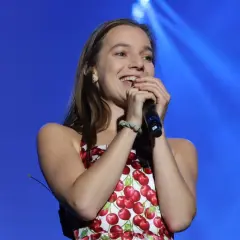 Sanah w sukience w wiśnie śpiewa na koncercie z niebieskim tłem.