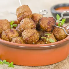 Polpette di tacchino dorate e succulente, cotte nella friggitrice ad aria, servite in una ciotola di terracotta con erbe aromatiche.