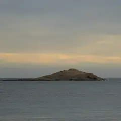 Isla de San Andrés, Almería, un islote rocoso en el mar con gaviotas posadas. Cielo nublado con tonos anaranjados.