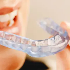 Persona sonriente sostiene una férula Invisalign transparente, lista para mejorar su sonrisa.