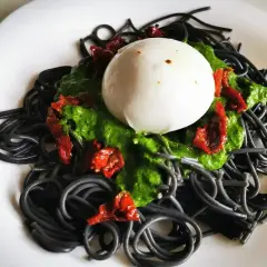 Czarny makaron z zielonym pesto, suszonymi pomidorami i kulką mozzarelli. Wygląda apetycznie!