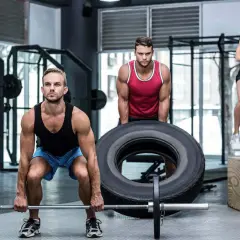 Trzech ludzi ćwiczy w siłowni. Mężczyzna podnosi sztangę, drugi przewraca oponę, a kobieta skacze na skrzynię. To jest crossfit, co to za trening!